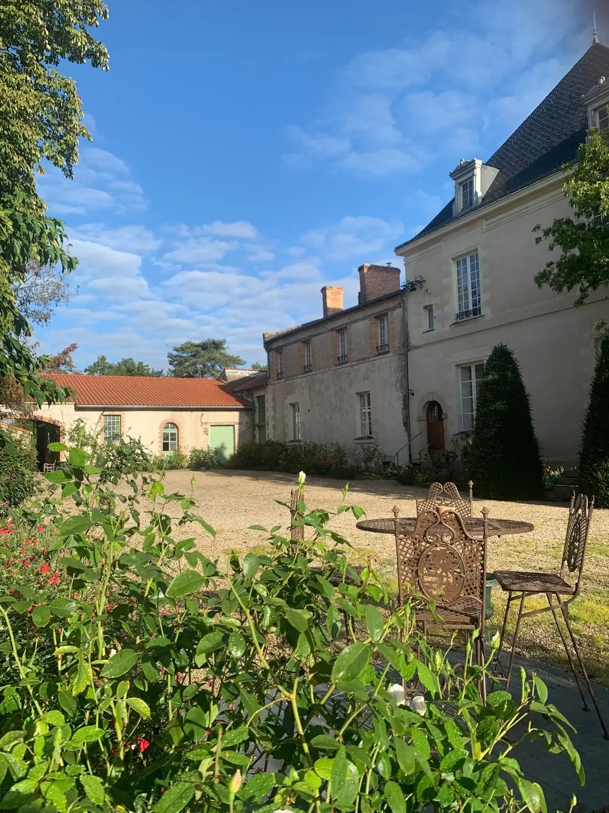 Façade du Château de la Bidière vue depuis le jardin fleuri et son mobilier en fer forgé