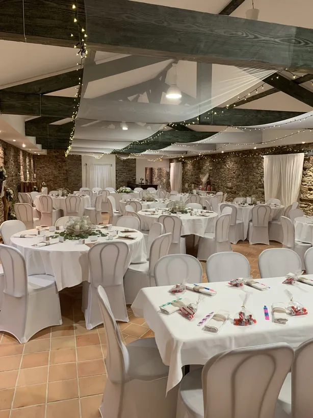 Salle de réception dressée pour un mariage, tables rondes et chaises housses blanches